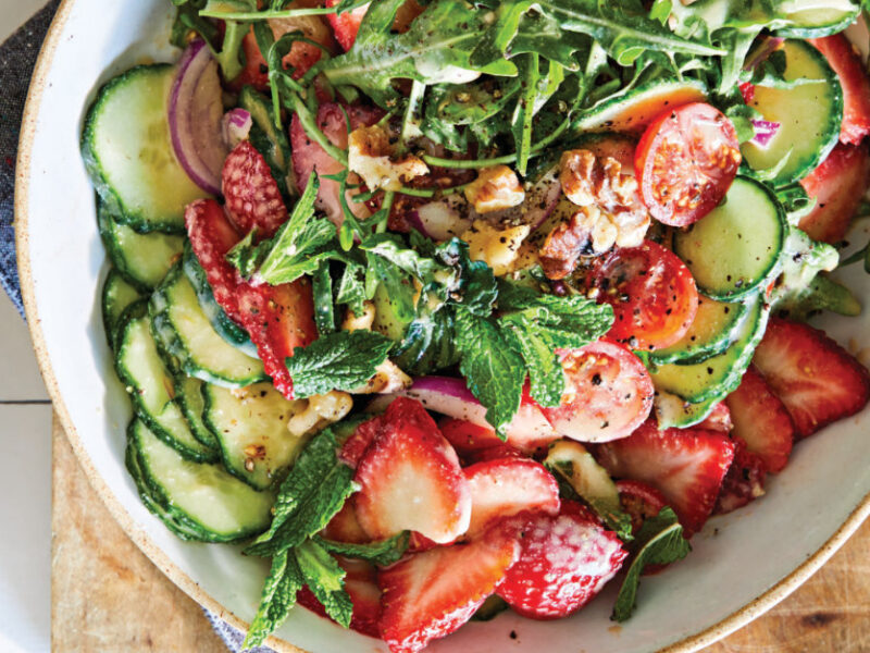 10-Minute Strawberry Cucumber Salad in a white ceramic bowl on a wooden chopping board and a blue cloth napkin