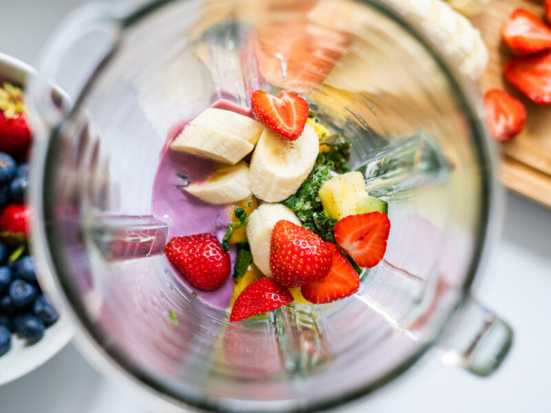 Top-down view into a blender with fruit smoothie ingredients inside of it