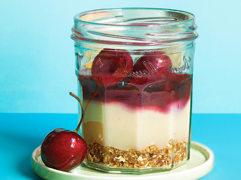 Mini Cherry Panna Cotta Parfaits on a small white plate with a fresh cherry on the side of the plate against a pale blue background