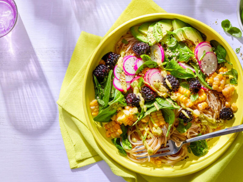 Easy Gourmet Noodle Bowls with Blackberries, Fresh Corn, and Avocado-Lime Dressing on a yellow cloth napkin against a lilac background