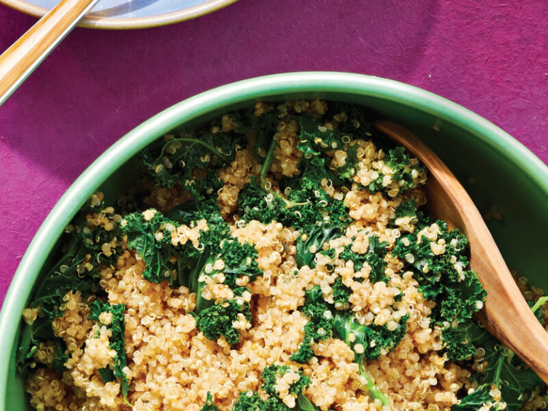 Herbed Quinoa with Kale in a green bowl with a wooden spoon against a bright pink background
