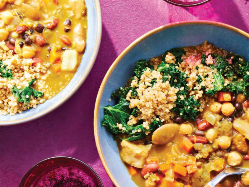 Two bowls of 4-Bean Jamaican Ital Stew with Herbed Quinoa and Kale on a dark pink background with a few sprigs of time