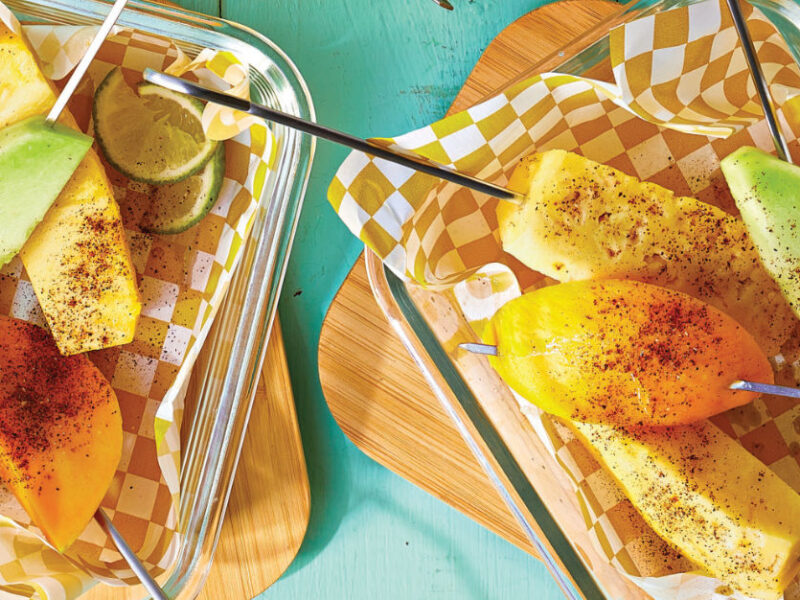 Two servings of Chili-Lime Fruit on a Stick on checked paper napkins in glass Tupperware containers