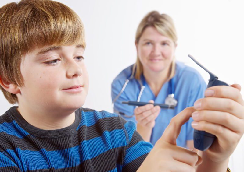 Boy looks at blood glucose monitor with nurse in the background