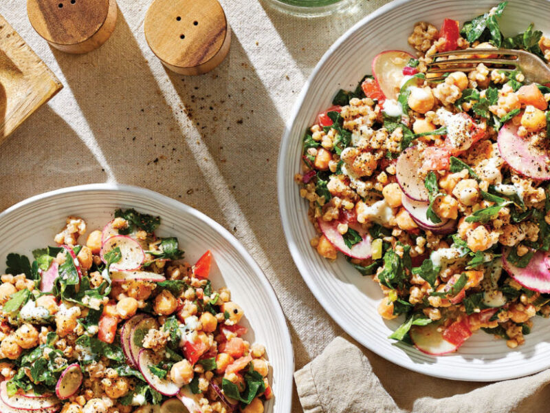 Two bowls of Buckwheat Tabbouleh with Chard, Chickpeas, and Creamy Garlic Dressing on a cream background with a fork in one of the bowls