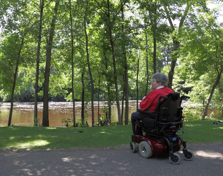 Woman with multiple sclerosis in an electric wheelchair by the bank of a peaceful river