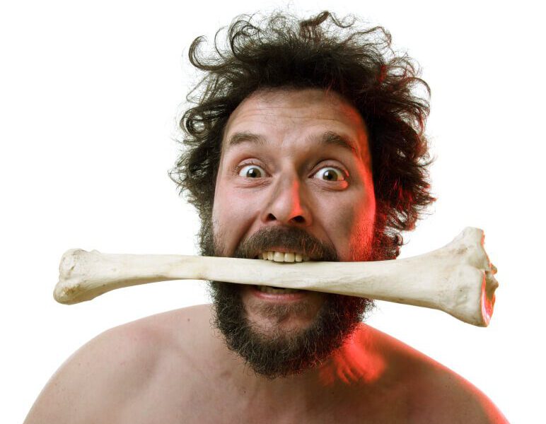 Shirtless, bearded man with a large bone in his mouth