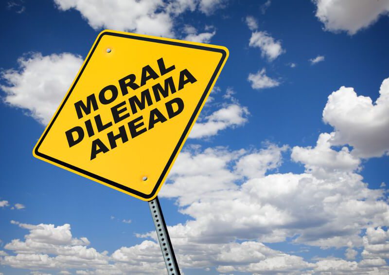 Looking up at a yellow road sign against the sky. The sign reads, "Moral Dilemma Ahead."