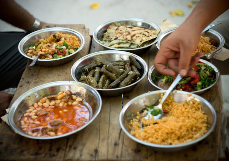 An unidentified man sitting at an outdoor table. On the table are many simple metal bowls will with healthy plant-based dishes