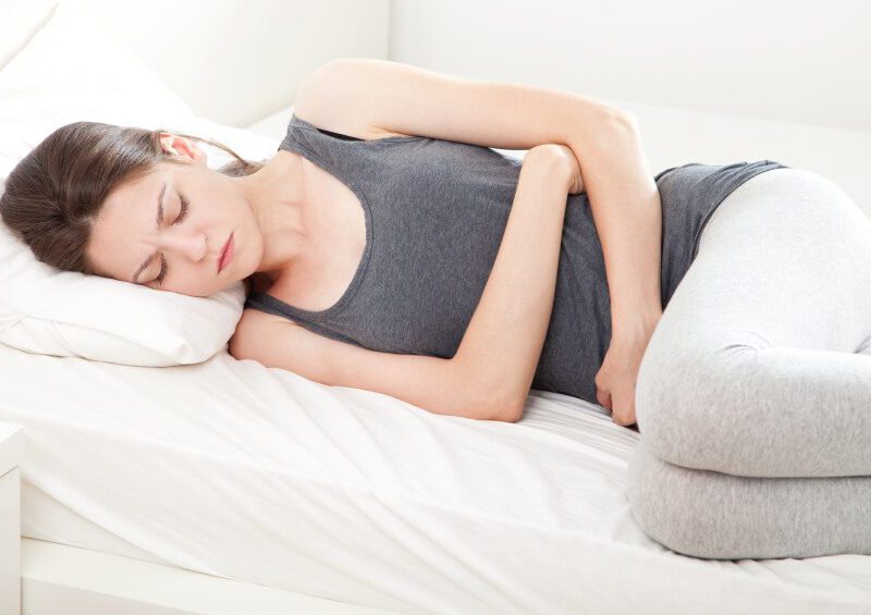 Unhappy young woman in pain lying on bed hands over her stomach