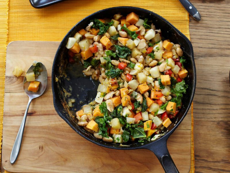 Vegetable White Bean Hash in a cast-iron skillet on a wooden chopping board