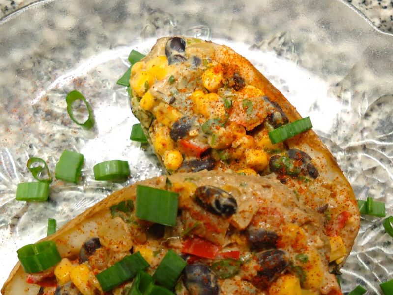 Two Southwestern Vegan Twice Baked Potatoes on a glass plate, garnished with green onion