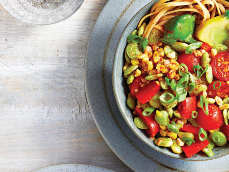 Summer Squash Succotash with Noodles in a blue-grey ceramic bowl sitting on a plate of the same color with a fork on the side