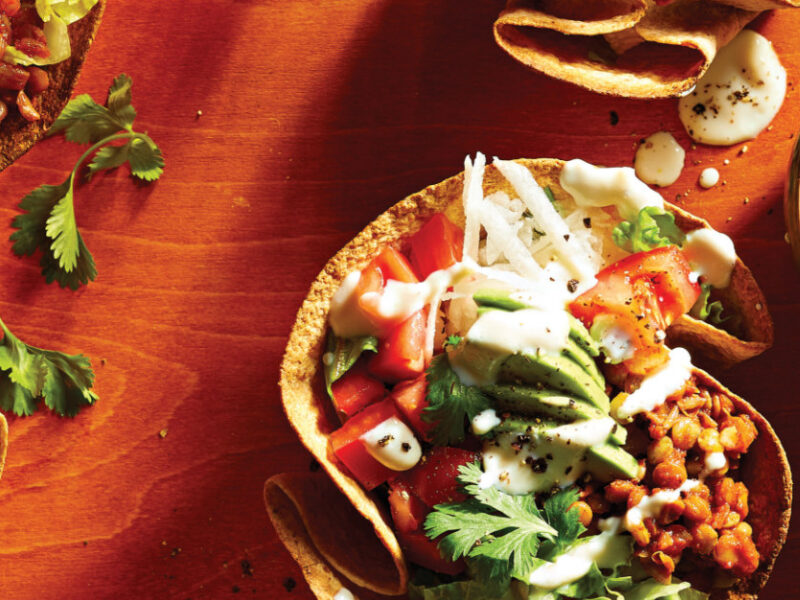 Lentil Taco Salad in Crispy Tortilla Bowls on a red tabletop next to a small bowl of lime crema