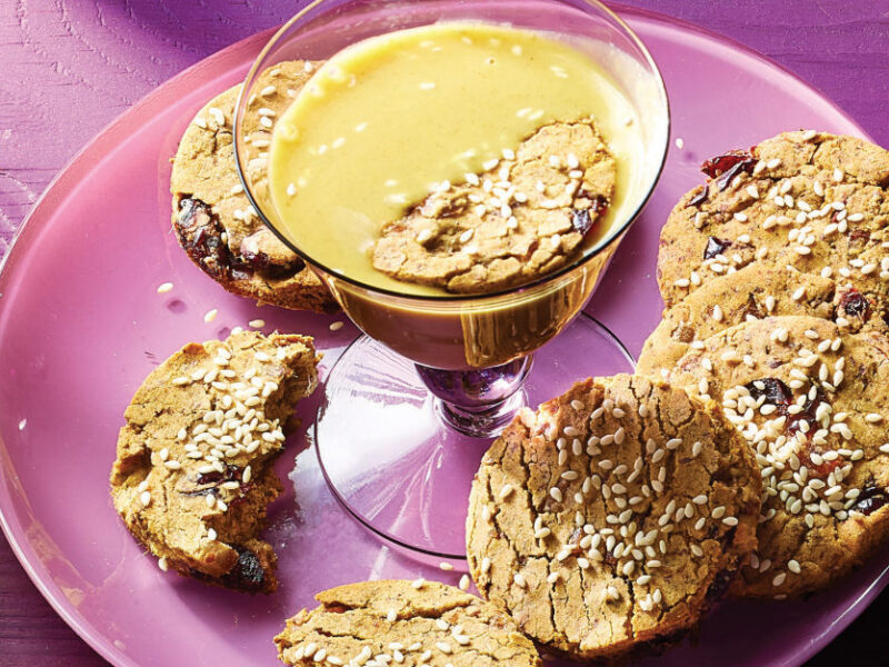 Sesame Date Cookies on a pink plate with a long stemmed glass filled with Golden Turmeric Milk in the middle of the plate