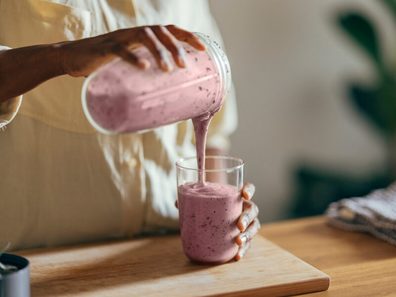 A woman pours a berry smoothie from a blender pitcher into a glass