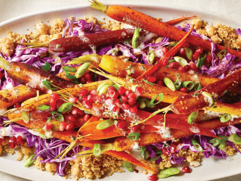 A large white platter of Harissa Roasted Carrot Salad with Couscous on a white table cloth