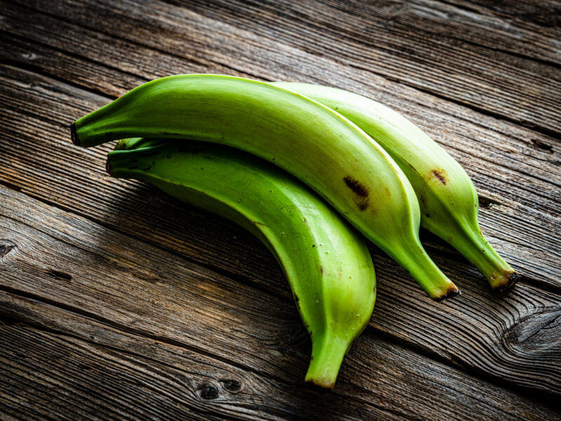 three green unripe plantains on a rustic wooden surface