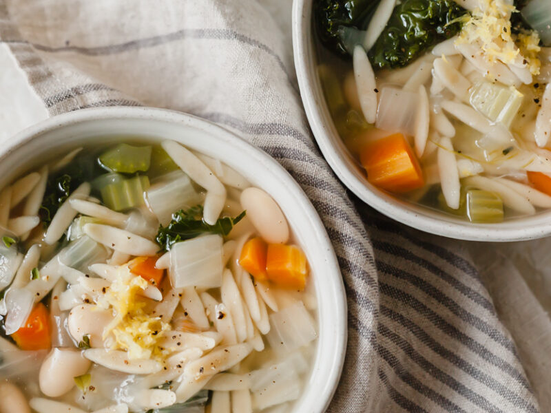 Two bowls of whole wheat orzo pasta soup with cannellini beans and kale