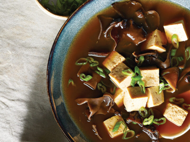 Chinese Hot and Sour Soup with Tofu in a blue ceramic bowl with a white spoon in the bowl
