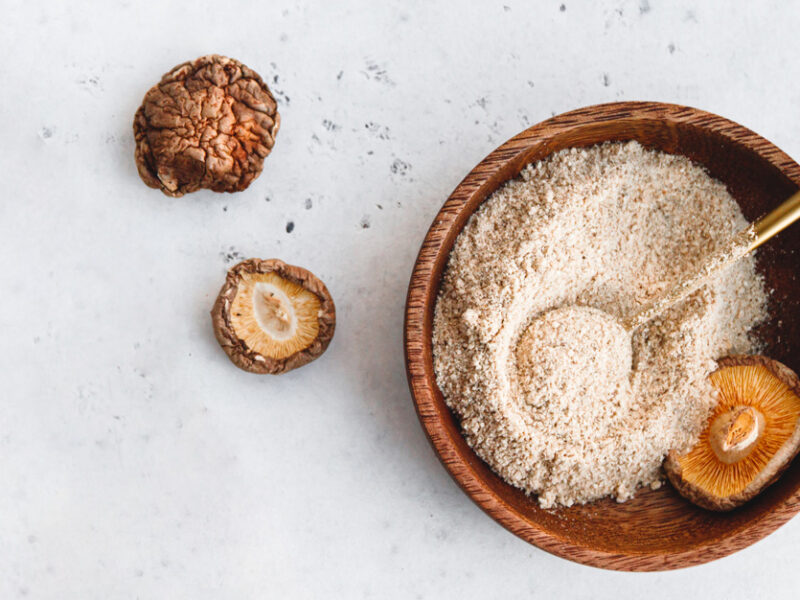 a top-down shot of a bowl of ground shiitake mushroom powder aka shroomami dust, an umami-rich salt-free seasoning you can make at home, shown beside a few dried shiitake on a marble counter