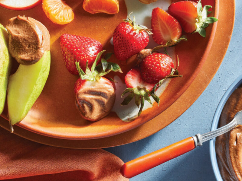 Raw Chocolate Caramel Dip in a small bowl next to a plate of bite-sized fruits