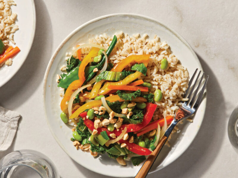 Low-Salt Veggie Stir-Fry over brown rice on two white dinner plates with a fork resting on the side of the plate