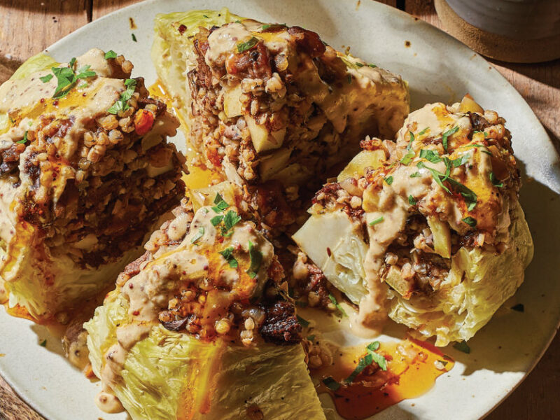 Stuffed Whole Cabbage with Kasha cut into quarters on a white plate, drizzle with Mustard Cream and Apple Cider Reduction