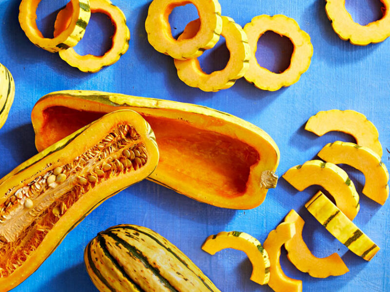 delicata squash cut into different shapes, including boats and rings, on a blue background