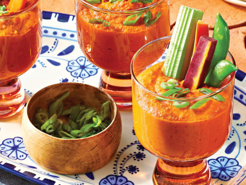 Three servings of Spicy Buffalo Hummus serve in glass glasses with a sturdy stem, with veggies sticks sticking out of them