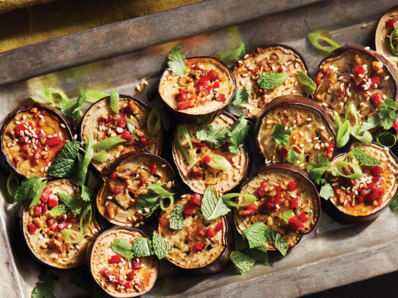 Vietnamese Eggplant with Cashews, Sesame, and Chile cut into 16 rounds, presented in a metal baking tray garnished with fresh mint leaves