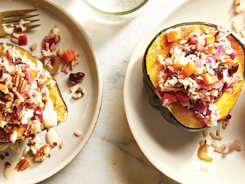 one Vegan Stuffed Acorn Squash half on a plate, drizzle with Creamy Tahini Sauce and fork on the side, next to a serving plate with two halves