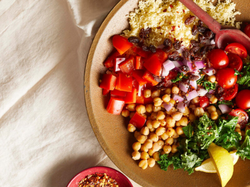 Lemony Moroccan Couscous Salad in a brown bowl with a wooden spoon on a cream-colored cloth napkin