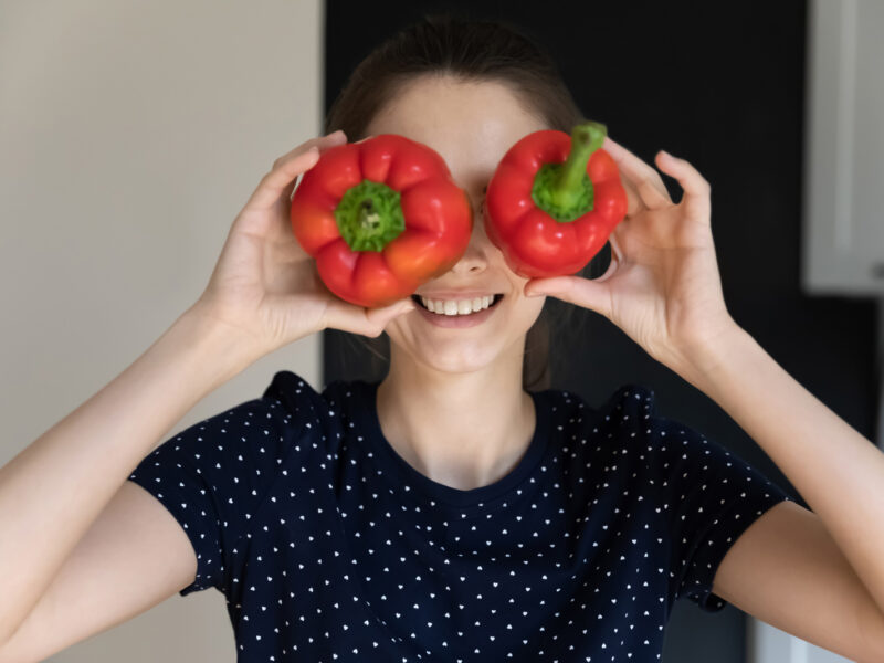 A young woman holds up two bell peppers to her eyes and smiles