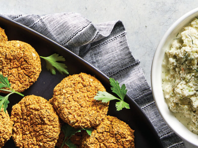 Baked Falafel in a black baking tray with a white bowl of Vegan Tzatziki Sauce to the side