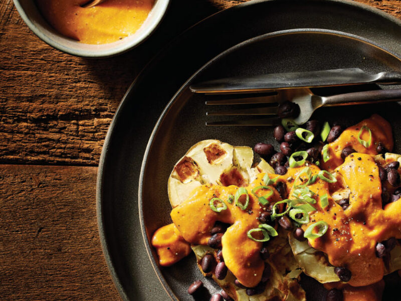 Easy Potato Waffles with Vegan Nacho Cheese Sauce on a black plate with a knife and fork and a small bowl of nacho cheese sauce off to the side