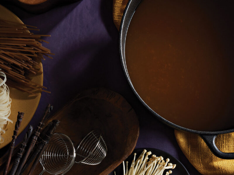 Sweet and Sour Vegan Hot Pot Broth in a cast iron pot next to dried soba and brown rice noodles