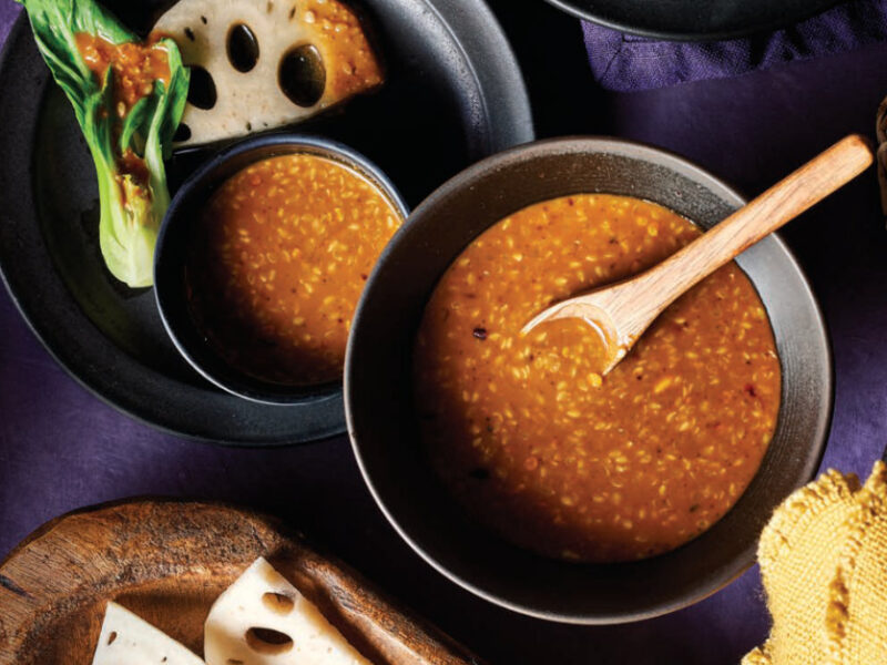 A bowl Peanut-Sesame Dipping Sauce next to a plate with a smaller bowl of sauce and bok choy
