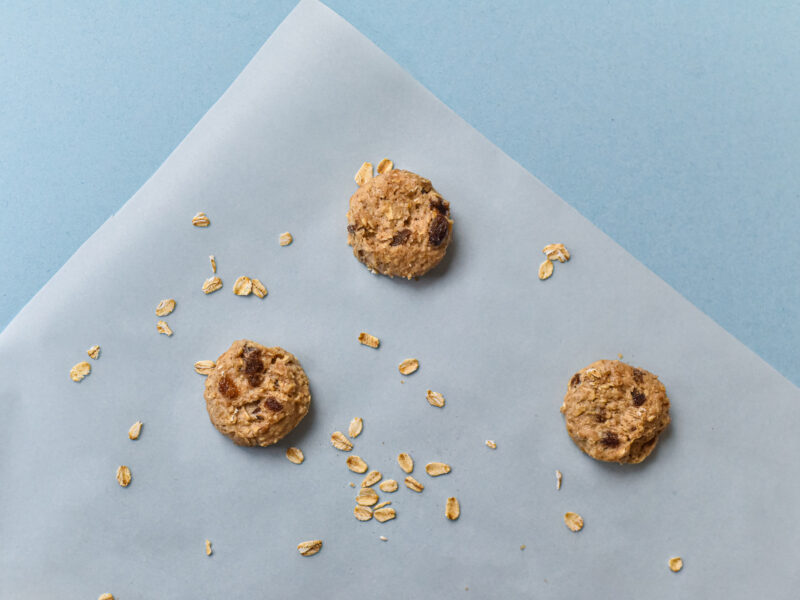 Three oat cookies on a parchment paper square with a blue background