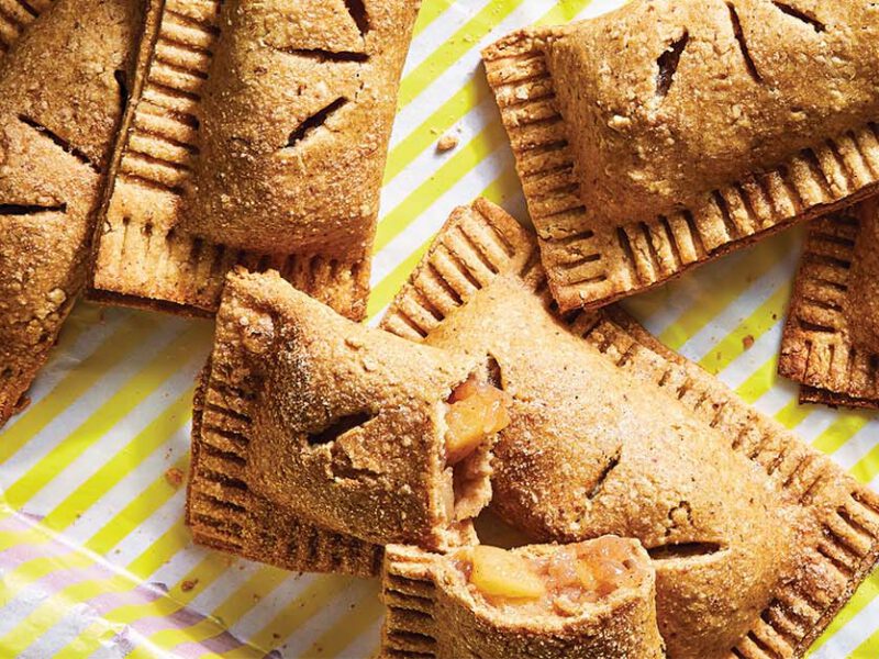 Vegan Cinnamon Apple Hand Pies on white and yellow striped paper on a red tray. One of the pies is broken showing the apple filling.