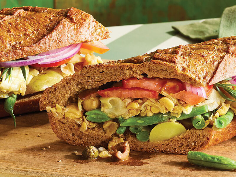 A close-up of two warm, stuffed baguette Vegan Niçoise Salad Sandwich (Pan Bagnat)