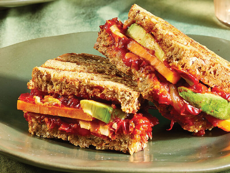 Avocado and Cherry Tomato Jam Panini cut in half with one half on top of the other, served on an earthy green ceramic plate