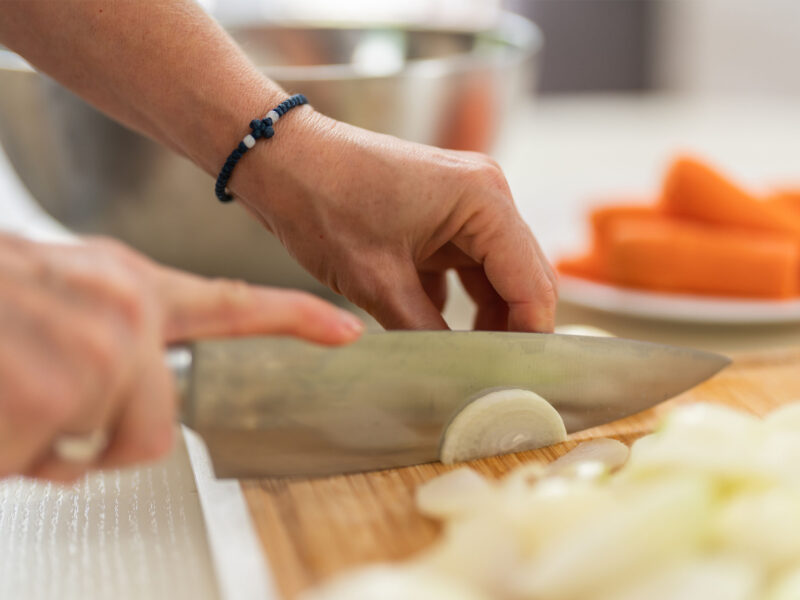 unidentified hands making mirepoix, cutting onion on a chopping board with a plate of carrots in the background