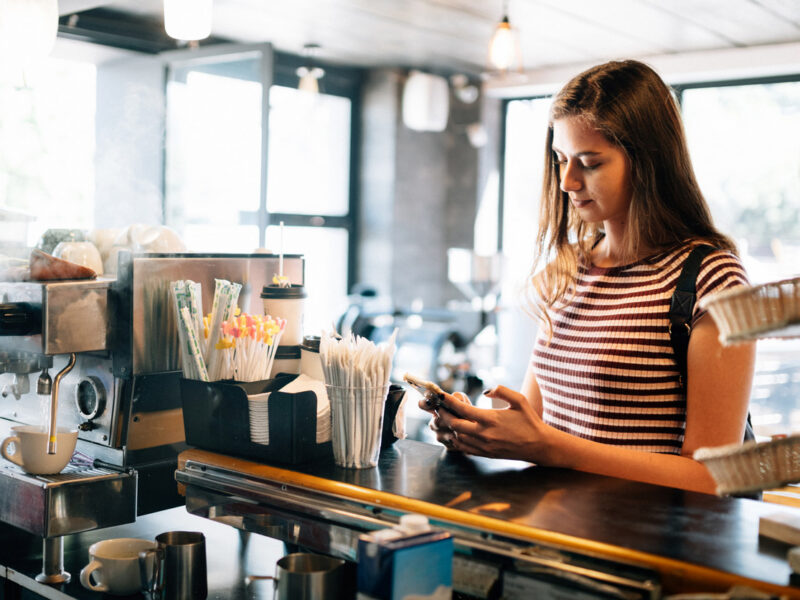 Young woman looks at her phone while waiting for her order at a chain coffee shop