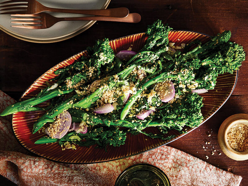 A red platter of Ginger-Sesame Broccoli Rabe Salad with shallots dotted throughout