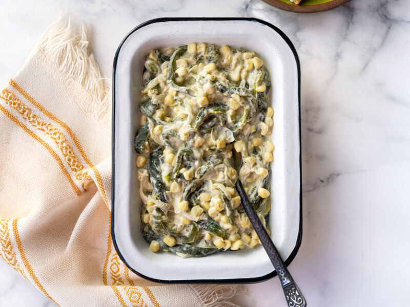 A white baking dish full of creamy poblano and corn filling, with a spoon in the dish
