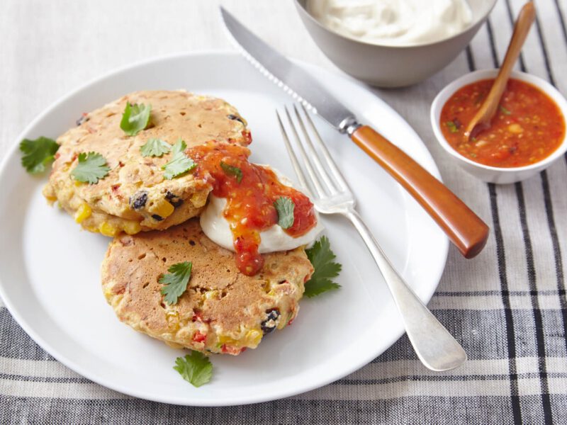 Two Corn and Black Bean Cakes with a dollop of vegan sour cream and a drizzle of salsa on a white plate