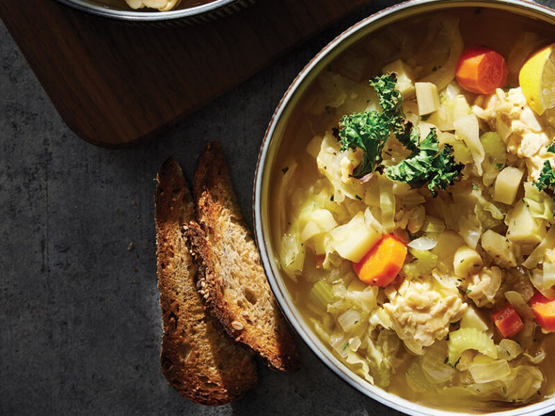 Cabbage Stew with Tempeh and Crispy Kale in a ceramic serving bowl with crusty bread on the side