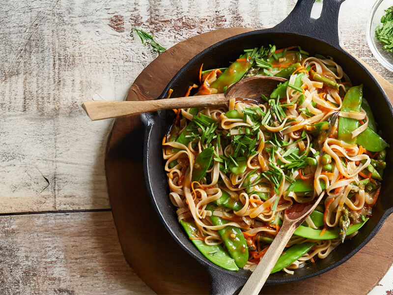 Stir-Fried Noodles with Veggies in a case-iron pan, with a small bowl of freshly cut chives to the side