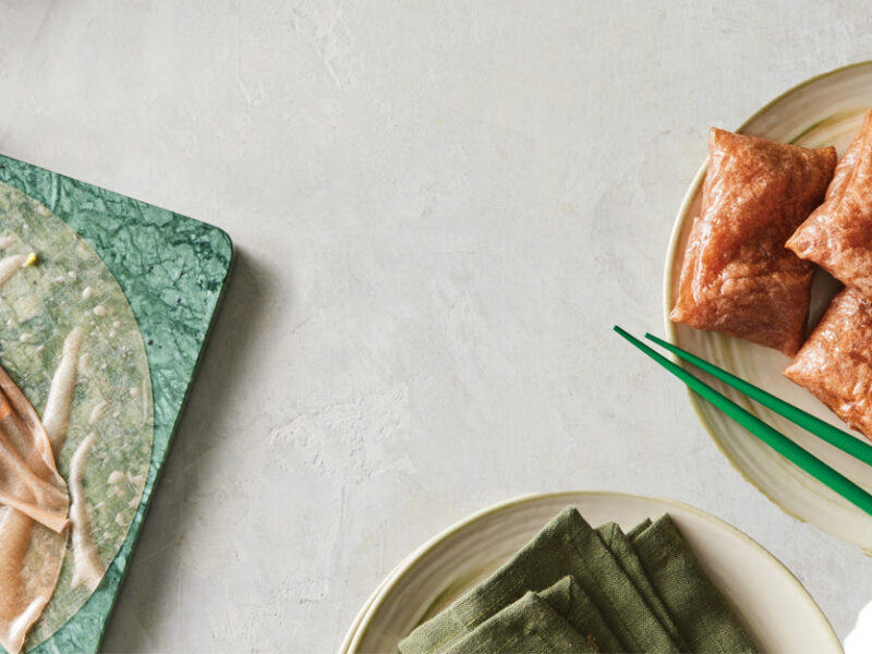 A plate of cooked Air-Fryer Rice Paper Dumplings on the right, and on the left you can see a dumpling partially wrapped on a green plate